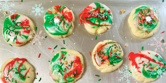 A collection of Christmas cookies on a baking sheet, their frosting is in tie dye swirl patterns of green and red with sprinkles