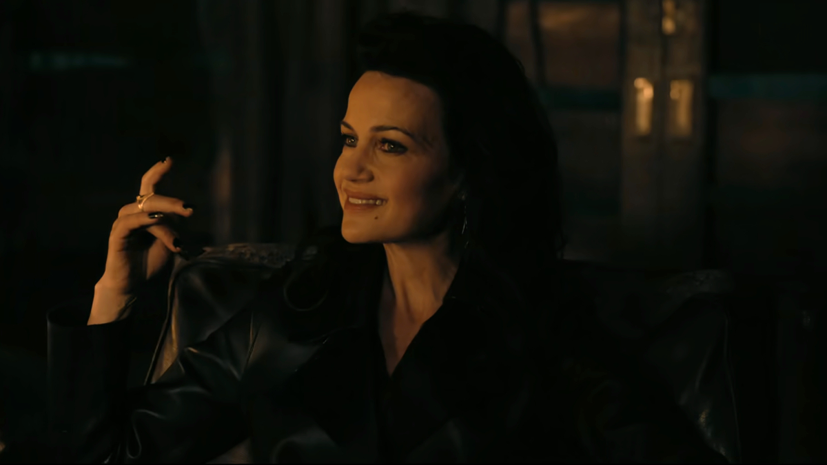 Carla Gugino sits in the dark wearing black leather and smiling.