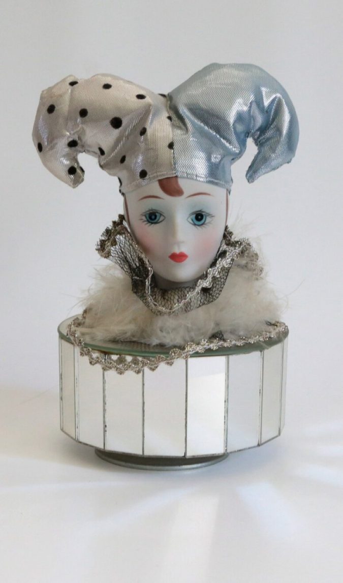 a porcelein harlequin clown head sitting atop a mirrored music box