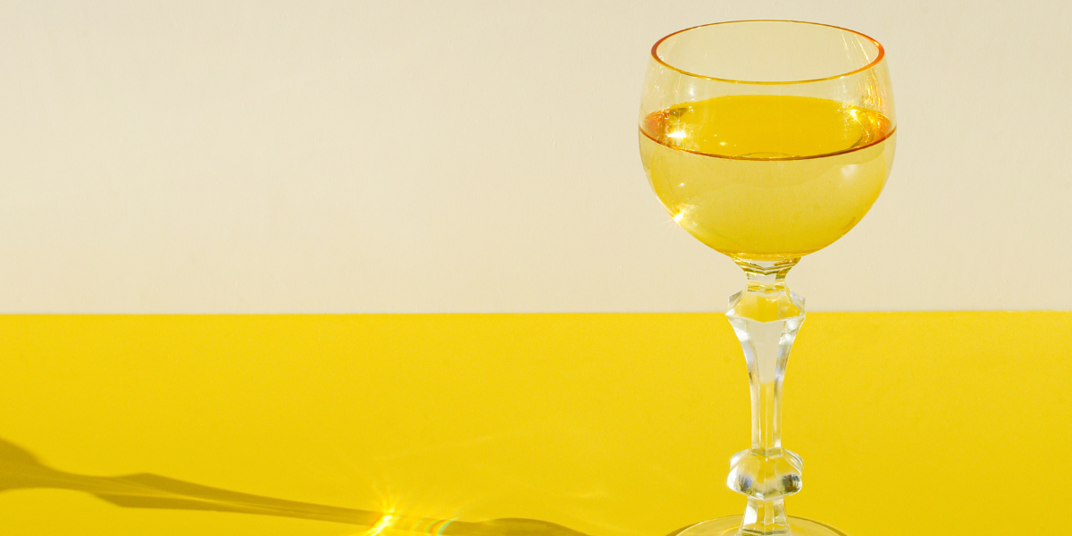 a glass of white wine against a bright yellow background