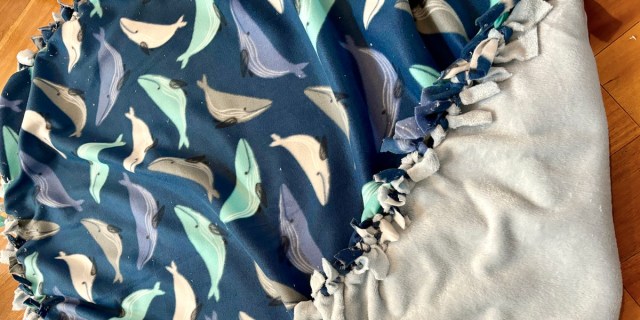 A DIY no-sew blanket in fleece fabric with blue whales on it, in a a close up photo.