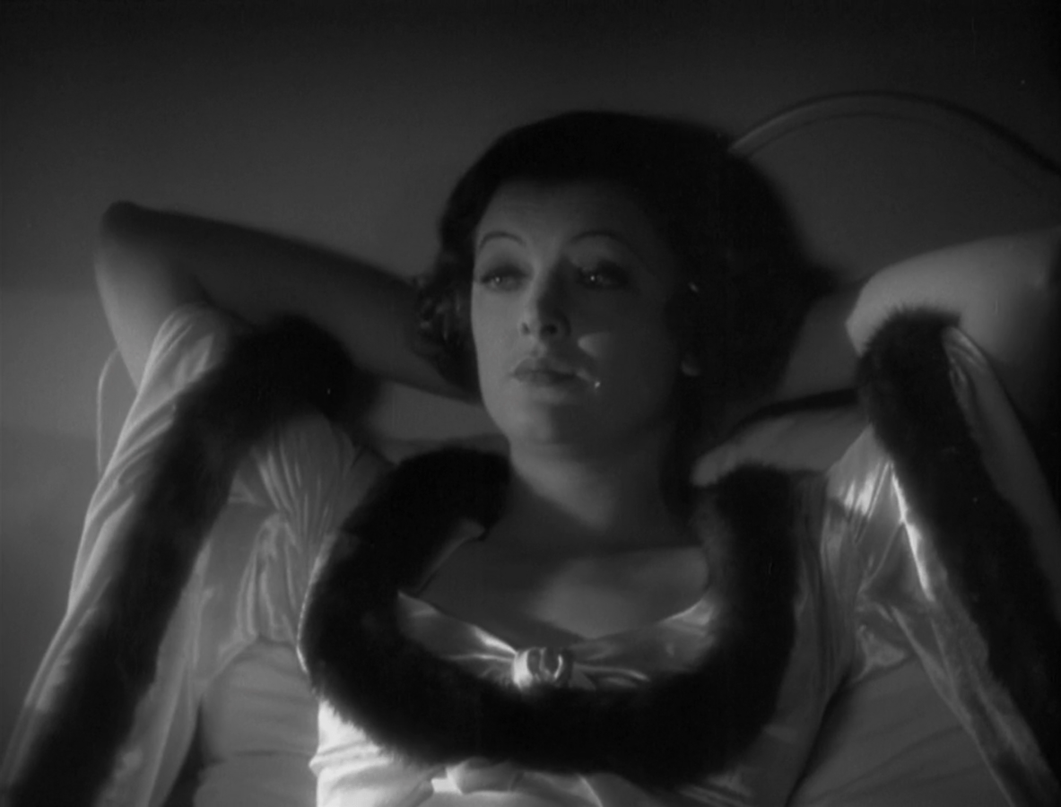 Myrna Loy leans back in bed with her hands behind her head