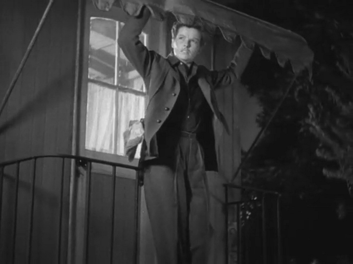 Katharine Hepburn dressed like a man leans on a porch