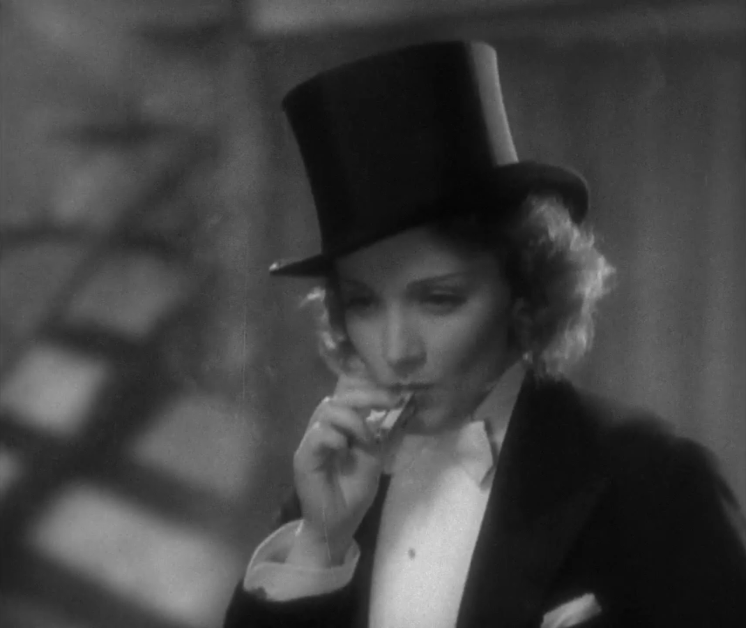 Marlene Dietrich smokes a cigarette wearing a top hat and a tux