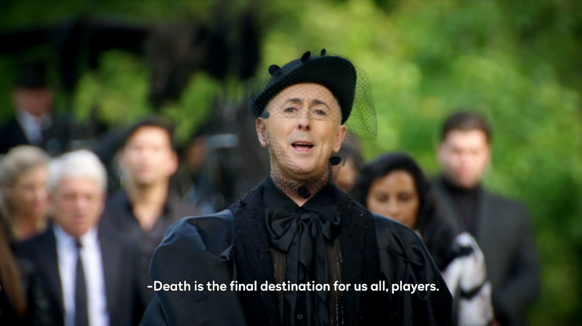 Alan Cumming, host of The Traitors Season Two, dressed all in formal black, leads the contestants in a funeral march, saying, “Death is the final destination for us all, players.” 