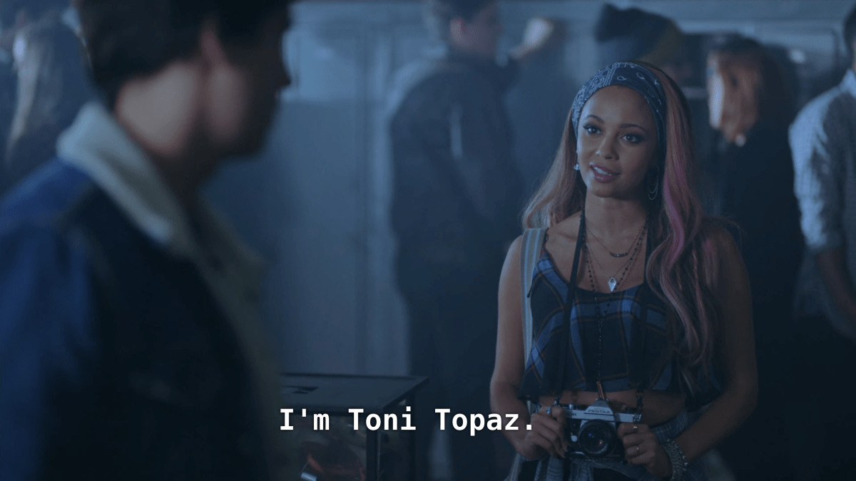 A girl with dyed hair holds a camera and talks to Jughead. "I'm Toni Topaz"