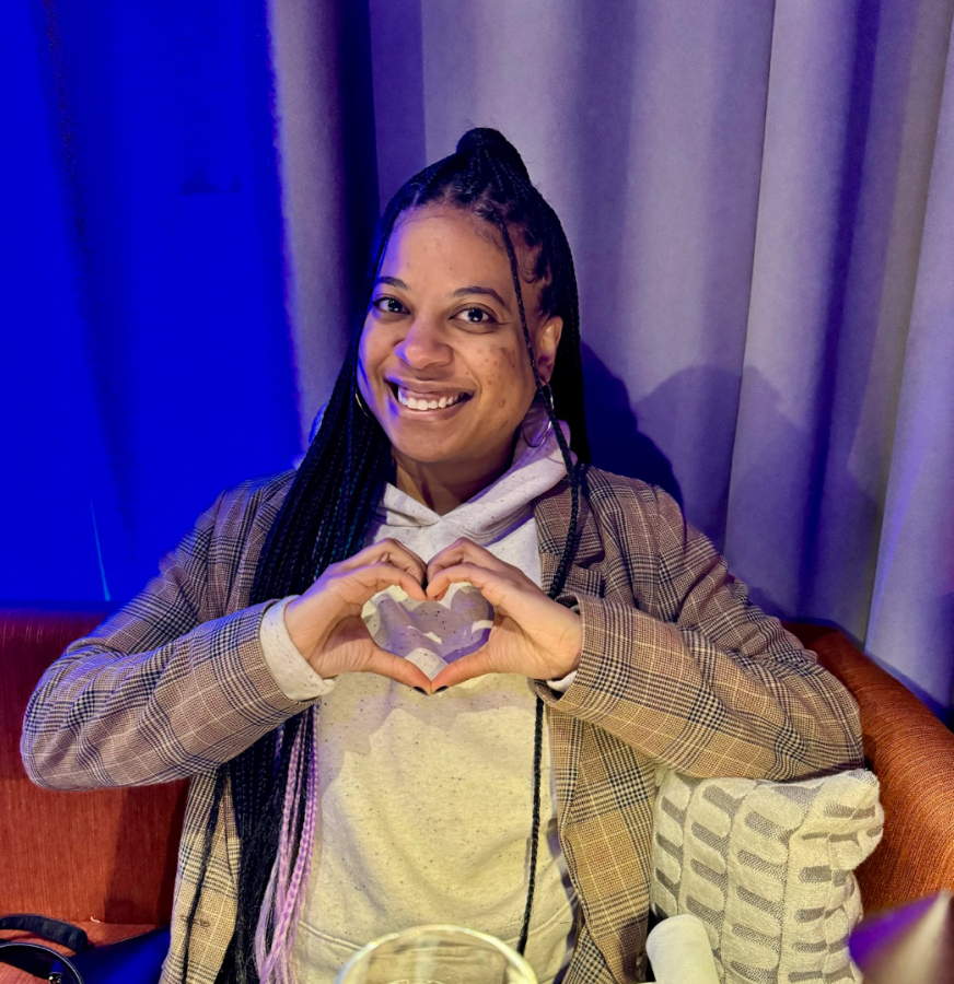 nic, a Black woman with long braids holds up her hands in a heart shape