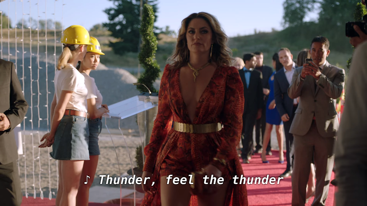 Alice Cooper walks down a red carpet in a revealing dress and a snake necklace as two women construction workers look on.