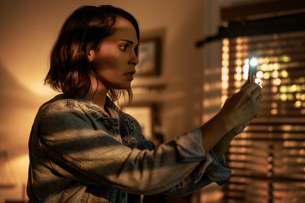 Hightown season three - Monica Raymund as Jackie shines a phone flashlight through the blinds at night