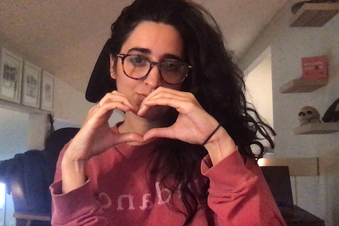 kayla, a southeast asian woman with long dark hair and glasses holds her hands up in a heart shape
