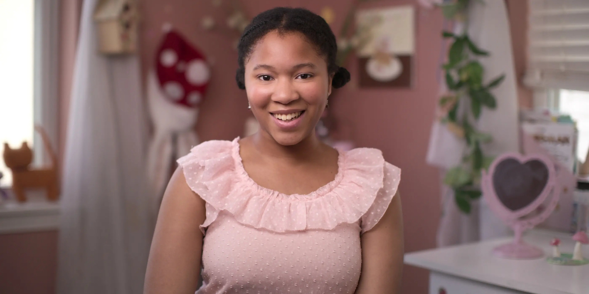 Love on the Spectrum queer: Journey, a teenage Black girl wearing a pastel pink top smiles at the camera.