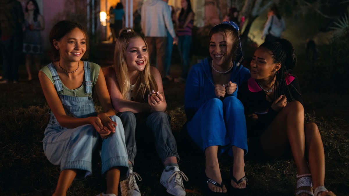 Four teenage girls sit next to each other smiling. 