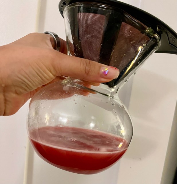 a pourover glass container with pomegranate juice dripping into it.
