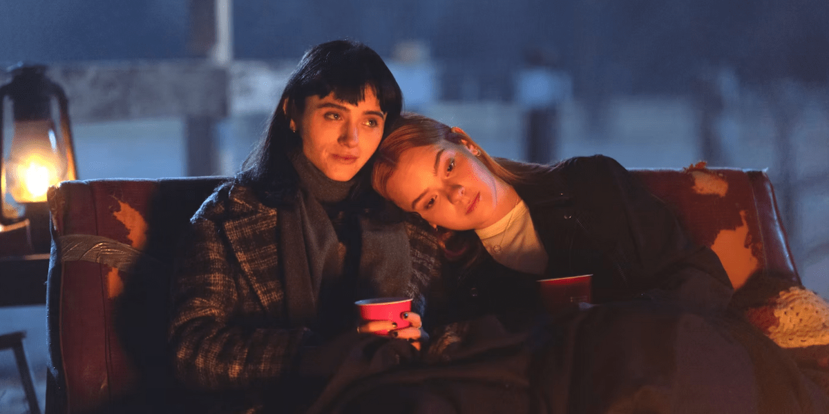 Natalia Dyer and Laurel Marsden in All Fun and Games sit on a couch together