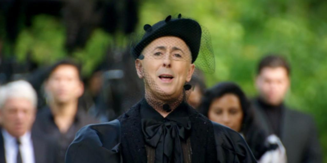 Alan Cumming, host of The Traitors Season Two, dressed all in formal black, leads the contestants in a funeral march, saying, “Death is the final destination for us all, players.”