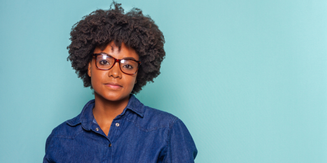 a Black woman with thick frame glasses and a denim buttondown