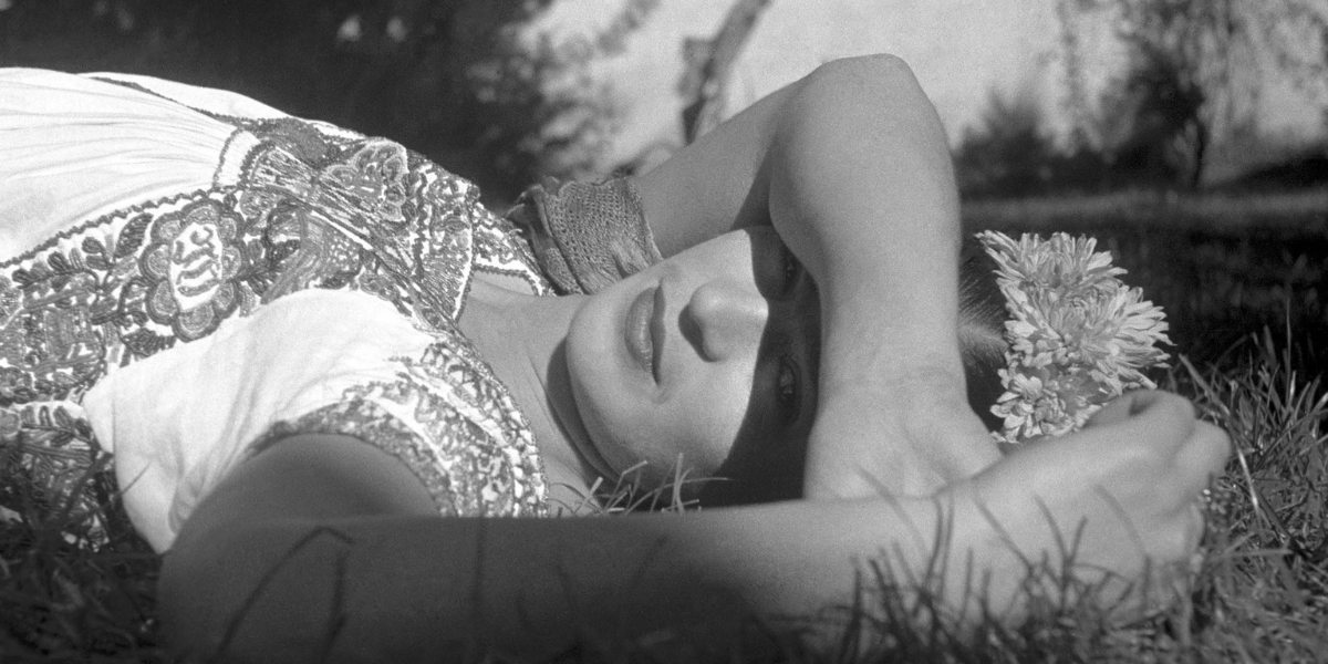 A black and white photo of Frida Kahlo leaning down in grass from the Frida documentary.