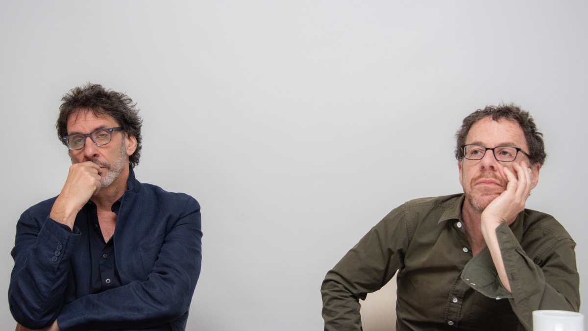 Joel and Ethan Coen rest their heads on their hands against a white backdrop