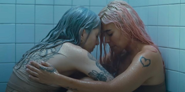 Two latinas, one with blue hair and one with pink hair, hold each other in the shower.