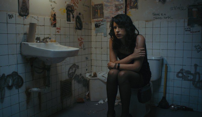 A Persian woman in her 20s is sitting on a toilet and she is very sad