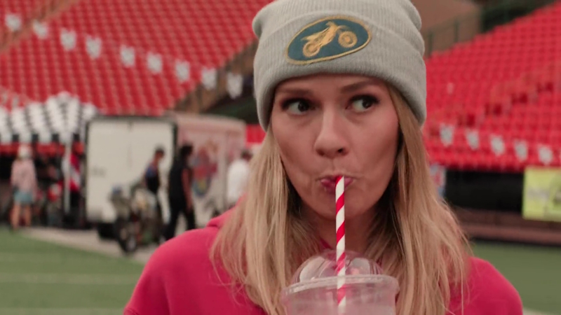 Kate Whistler in a red hoodie with grey beanie, slurping on an Icee straw.