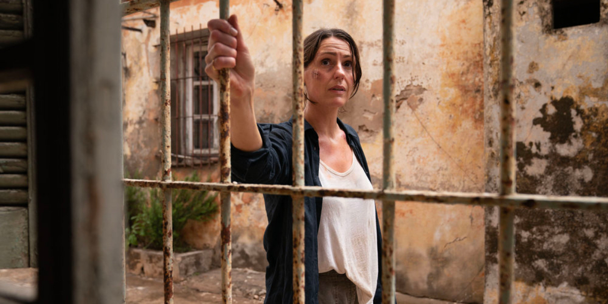 Vigil season two feature image - Suranne Jones stands with a beat up face gripping a jail door.