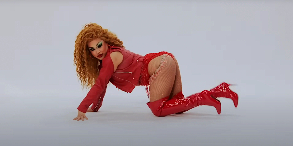 Drag race 1605: Morphine poses with a curly red wig and all red leather outfit with her ass up in the air.