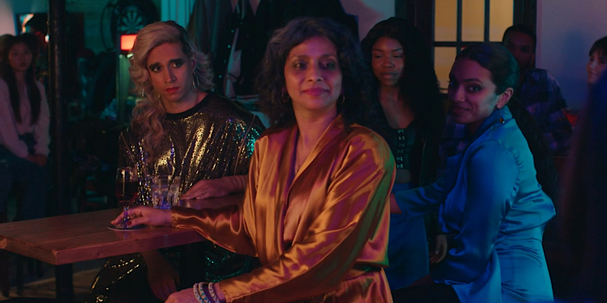 How to Fail as a Popstar: Vivek Shraya sits at a table with Ayesha Mansur Gonsalves and Nadine Bhabha as they watch a musician perform.
