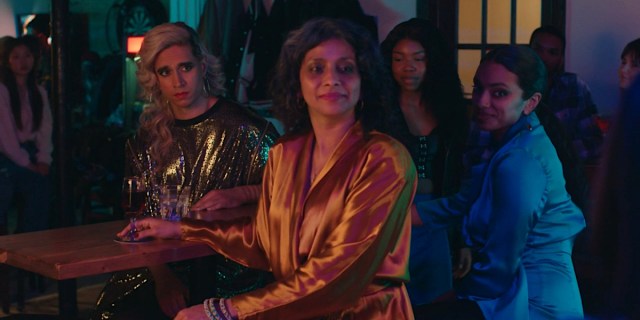 How to Fail as a Popstar: Vivek Shraya sits at a table with Ayesha Mansur Gonsalves and Nadine Bhabha as they watch a musician perform.