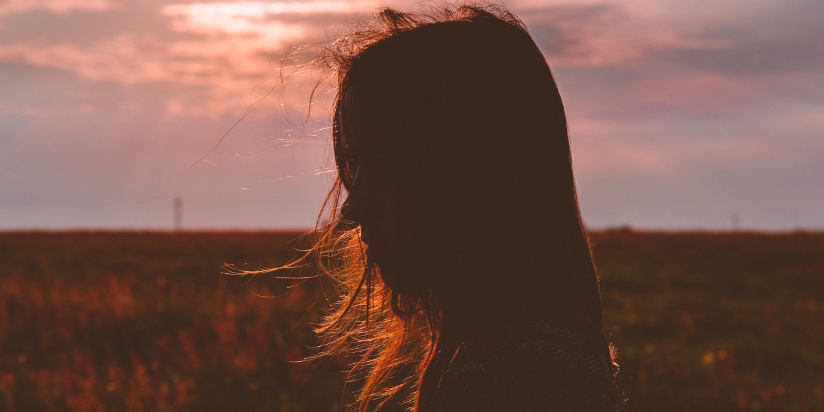 a woman alone in a field with wind swept hair