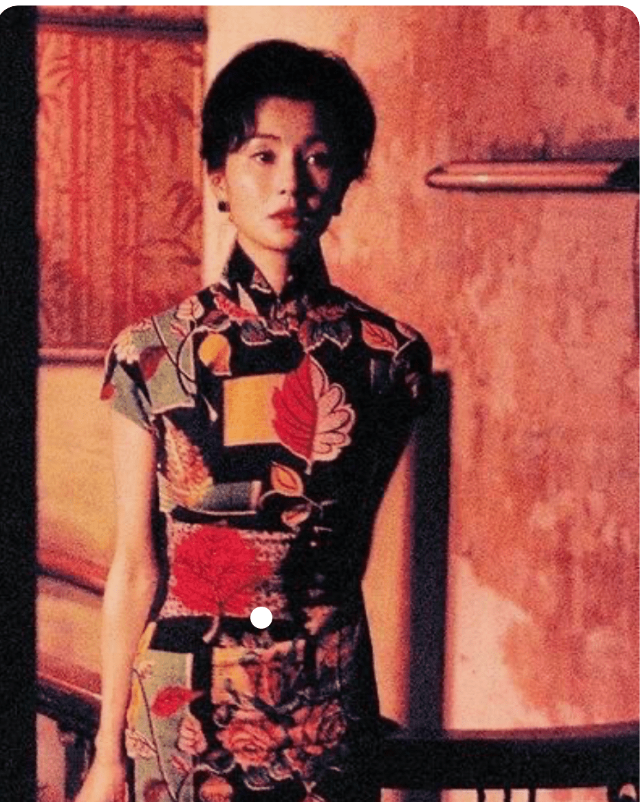 A still from In the Mood for Love shows an Asian woman in a dress that has various warm shades of brick, burgundy, peach, and gold