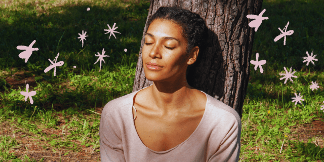 a Black woman sits with her head against a tree, closing her eyes in the sunshine