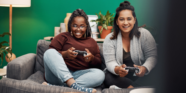 two women play video games on a couch together