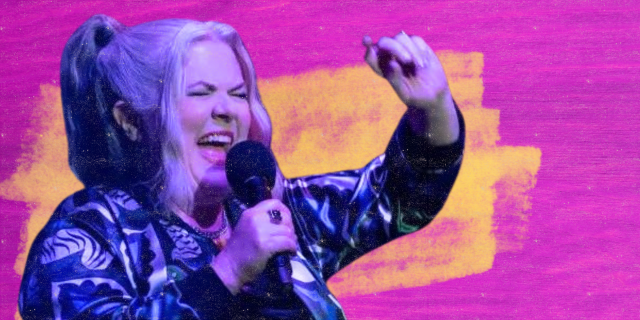 Girls5Eva season three: Paula Pell sings into a microphone with an arm in the air against a pink and yellow background.