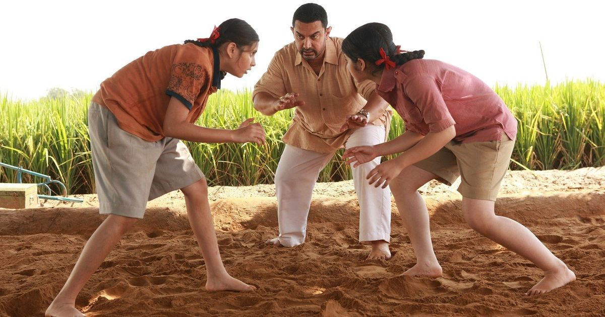 Two girls get ready to wrestle as their coach stands between them in Dangal