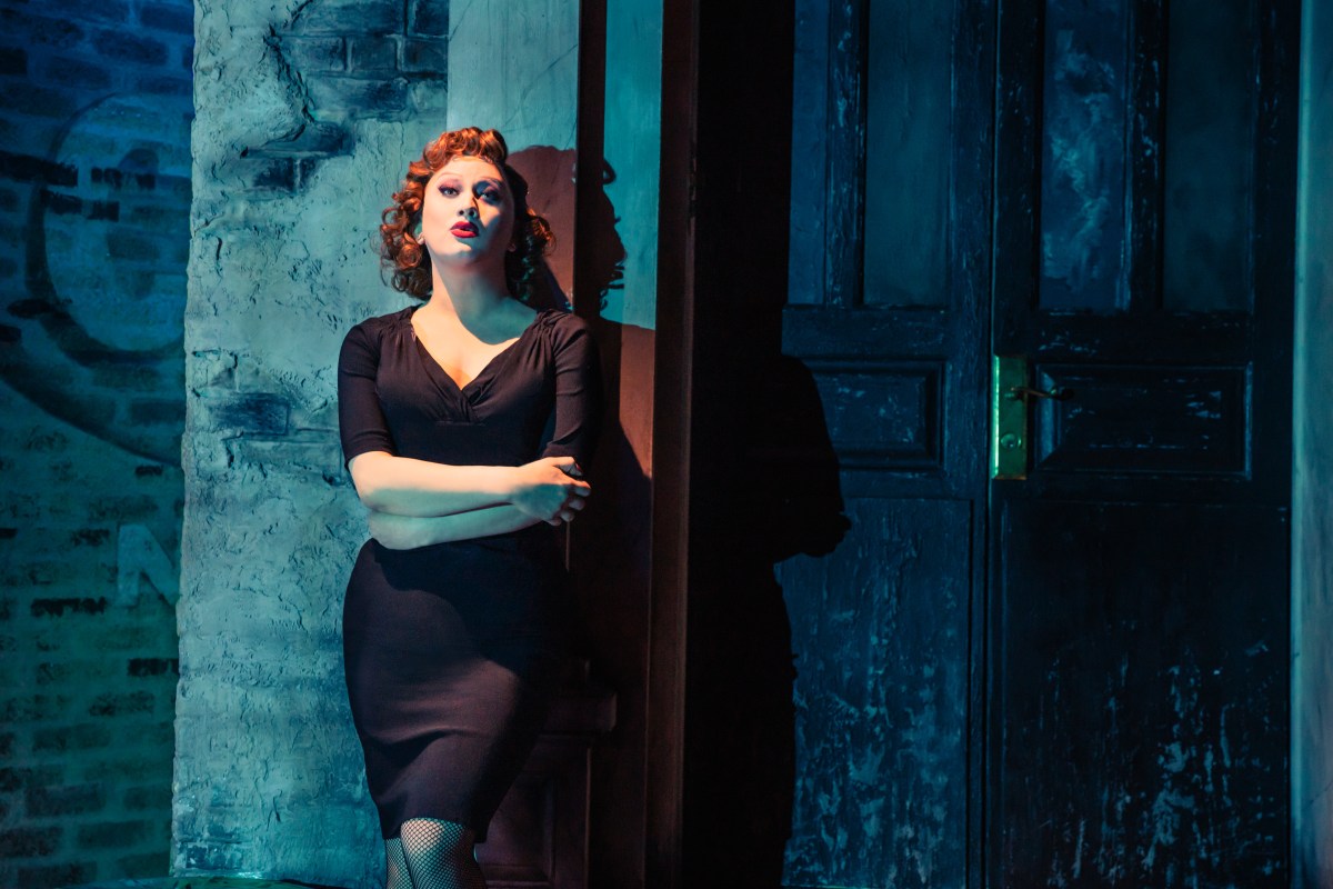 Jinkx Monsoon as Audrey in Little Shop leans against a wall in a tight black dress.