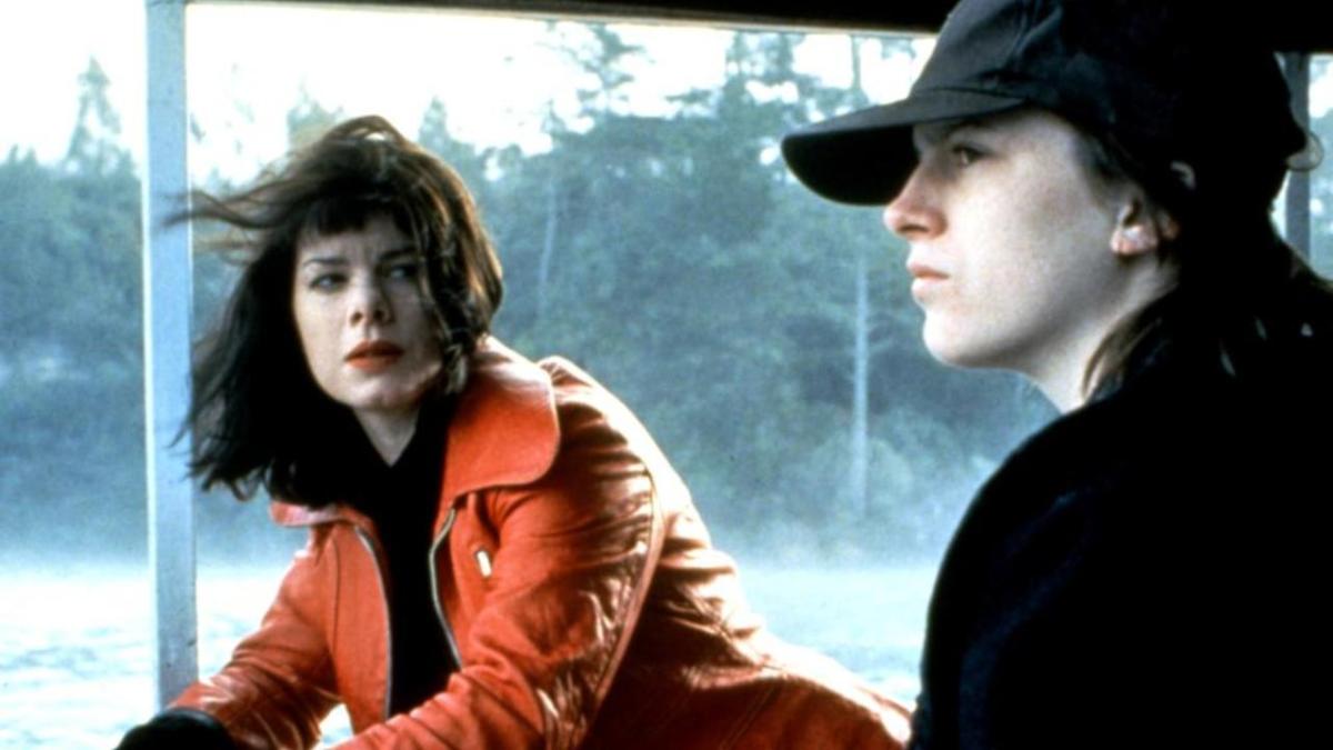 Marcia Gay Harden in a red jacket looks at Caitlin Bossley in a baseball cap, a river behind them.