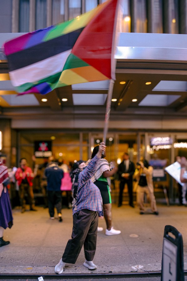 a protestor waves a flag that represents the Palestinian flag and the gay pride flag