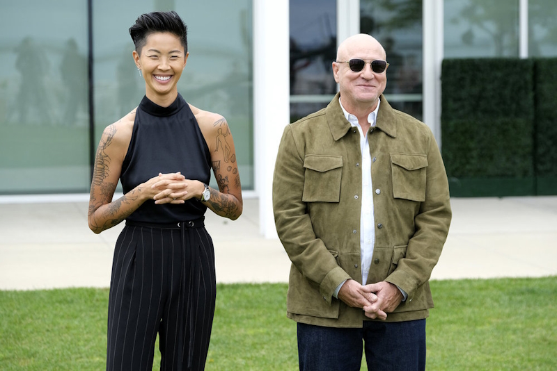 Kristen Kish stands next to Tom Colicchio (L-R). She's wearing black pinstripe pants with a black sleeveless blouse.