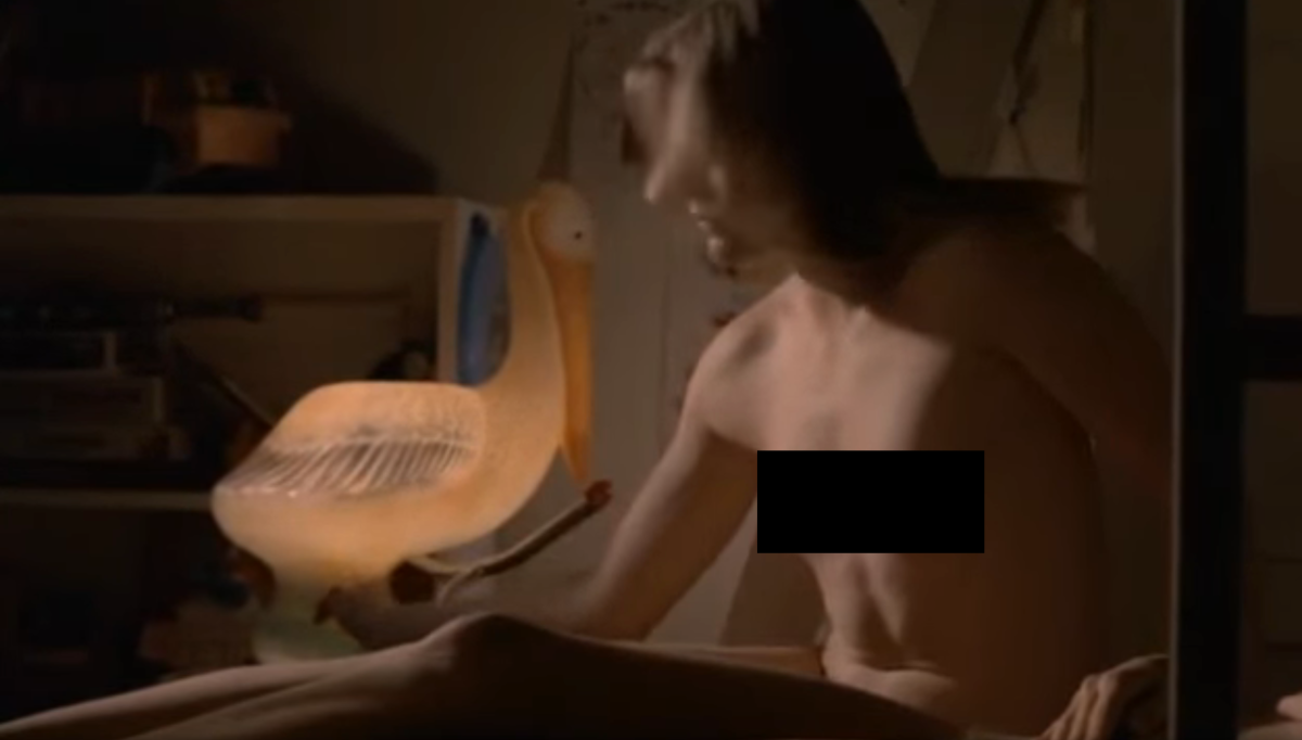 Chris sits up naked (censored) next to a glowing pelican lamp.