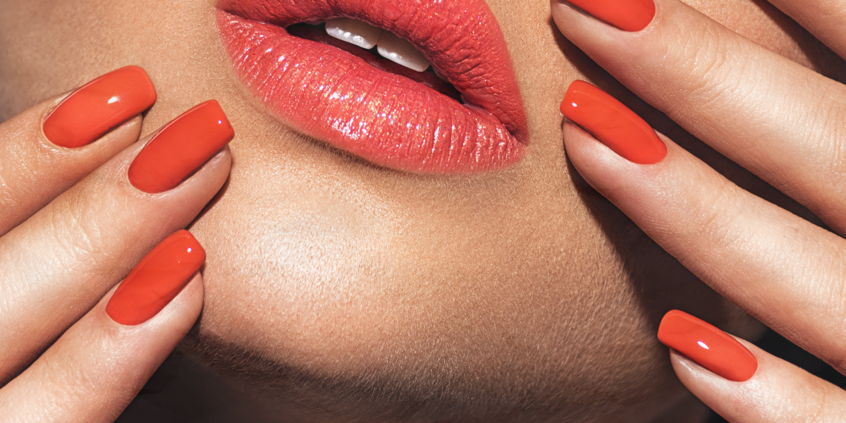 A close up of a woman's face with matching reddish-orange lipstick and nails.