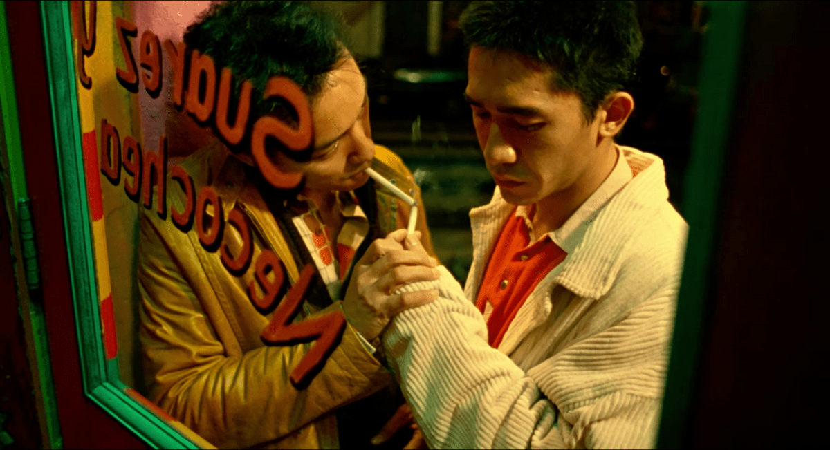 Tony Leung Chiu-wai and Leslie Cheung light each other's cigarettes leaning against a window.