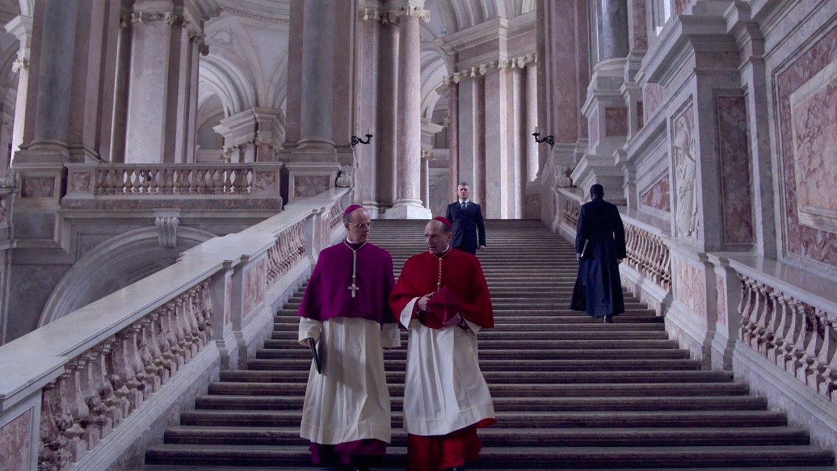 Brían F. O'Byrne and Ralph Fiennes walk down a large Vatican staircase in Conclave