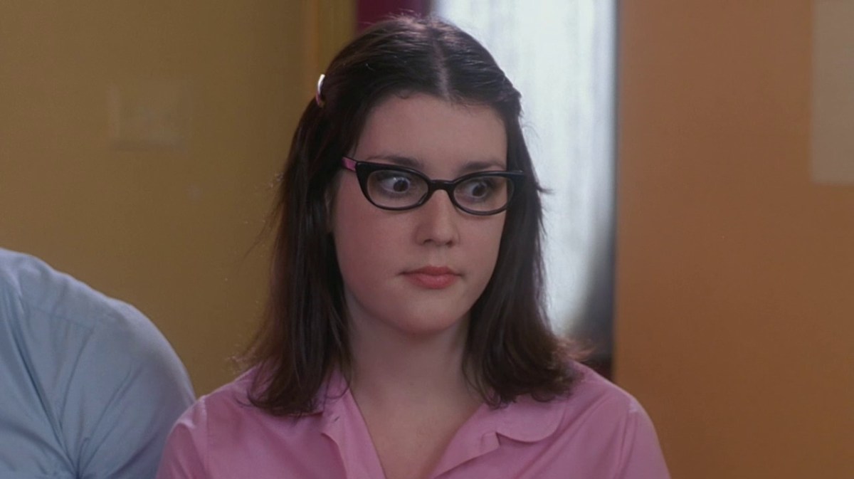 Melanie Lynskey in a pink shirt and black glasses.