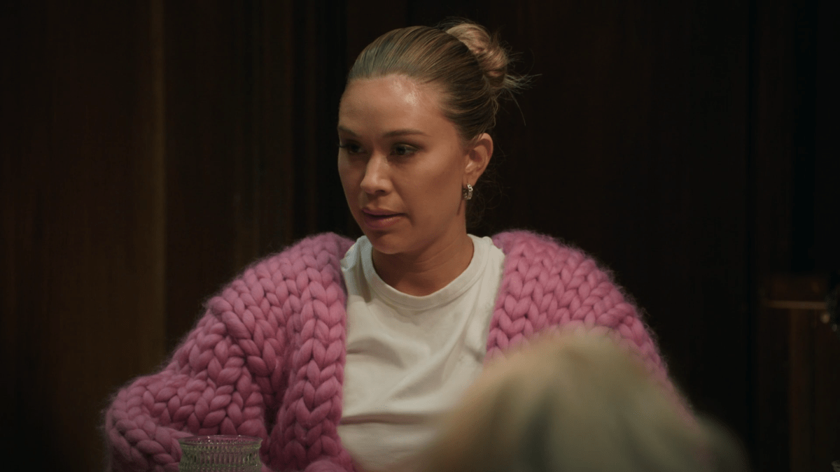 Gabby sits at the roundtable in a big pink sweater and a white t-shirt