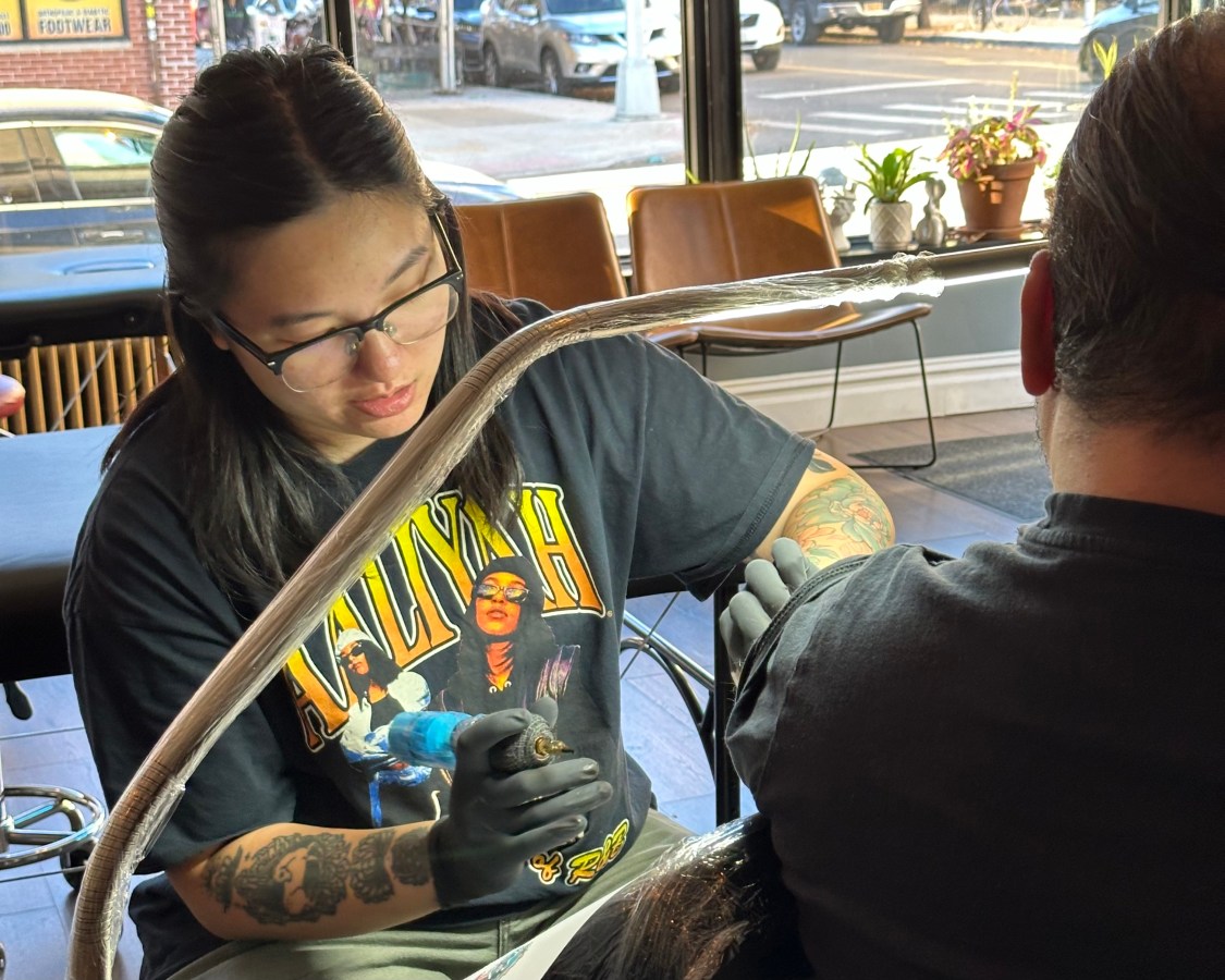 Tiffany Lai works on a tattoo while wearing an Aaliyah shirt