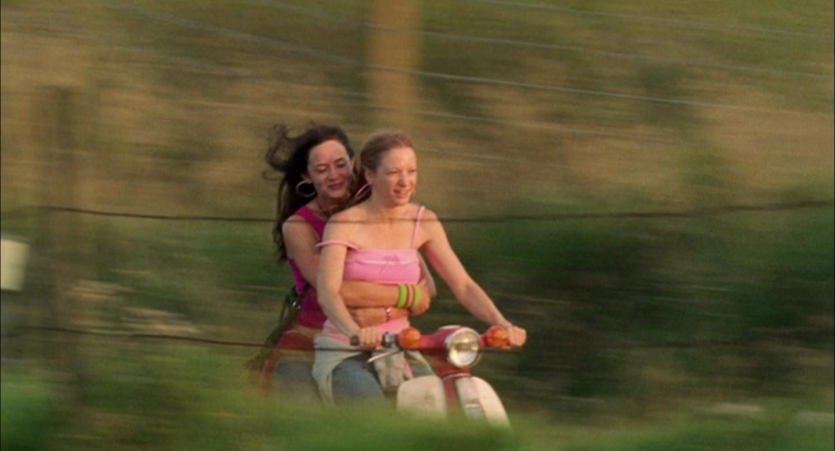 Two girls ride on a vespa in the summer time