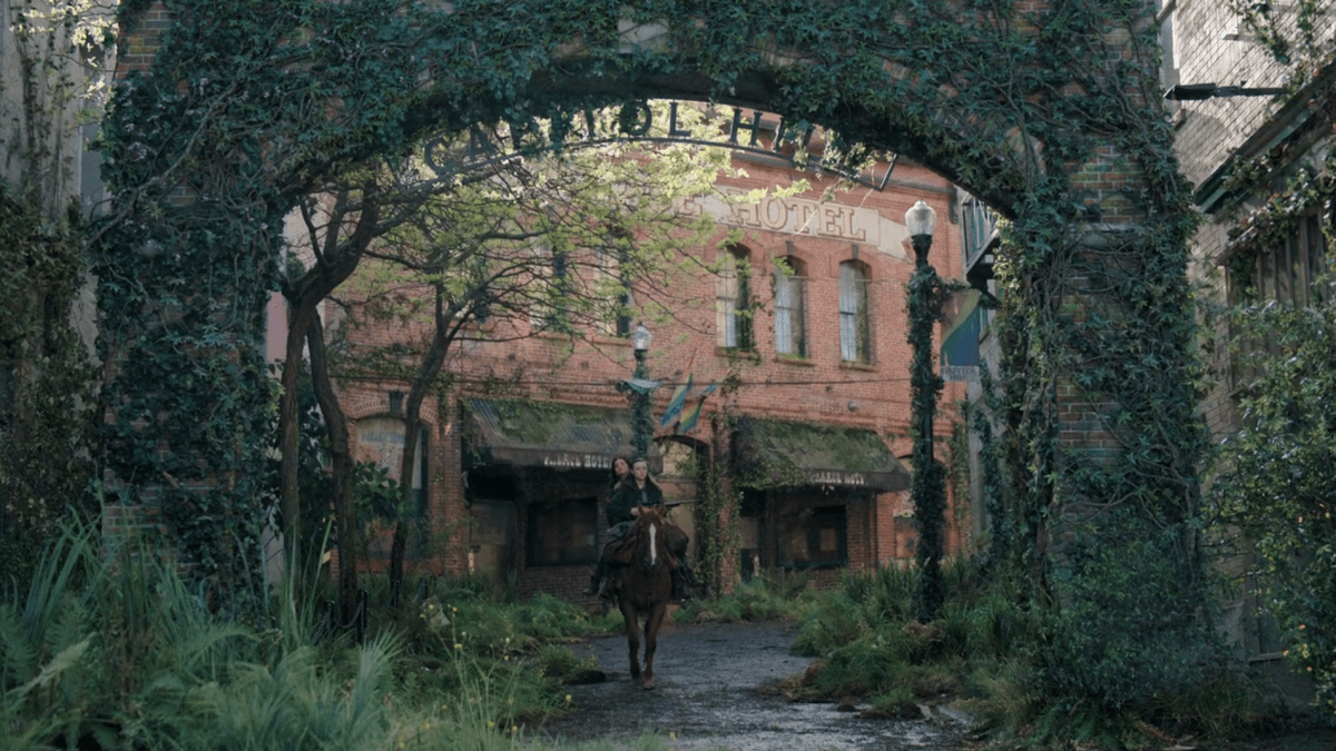 The Last of Us 204: Ellie and Dina ride on horseback through the gates of Capitol Hill, pride flags in the background
