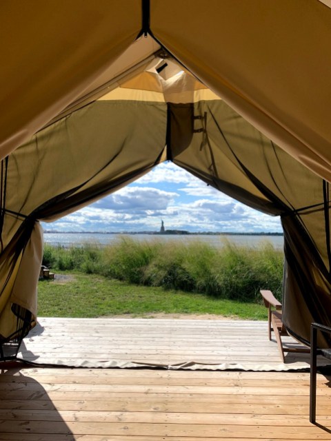 a canopy tent opens and a wooden deck is outside of it, with the statue of liberty in the distance