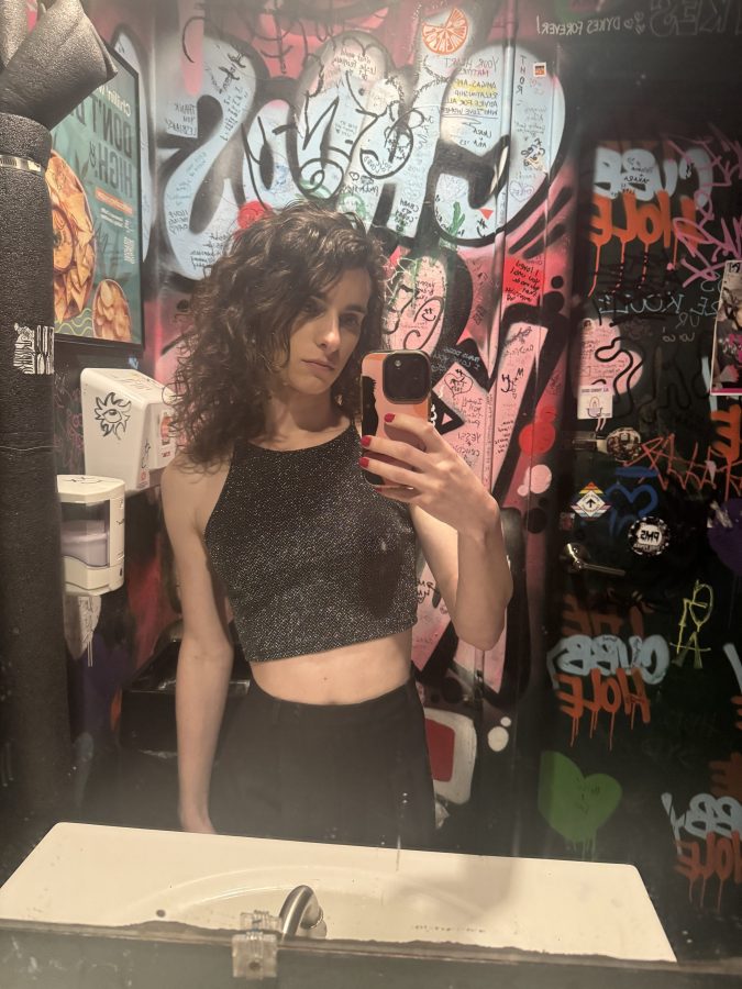 Drew takes a bathroom selfie wearing black pants and a shimmery black top